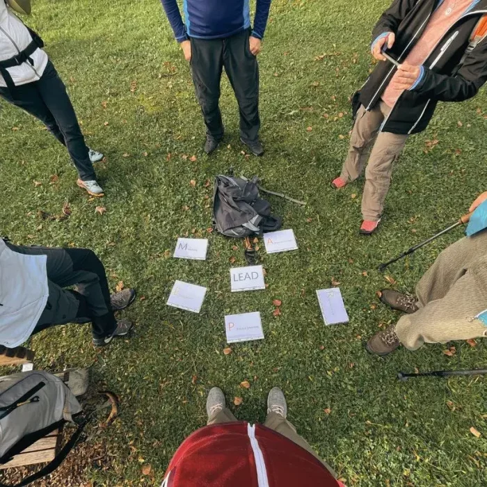 Sechs Personen stehen auf einer Wiese im Kreis. Vor Ihnen liegen Sechs einlaminierte Karten mit Text drauf.